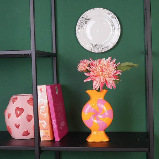 De oranje gestreepte vaas in een zwarte metalen kast tegen een groene muur.