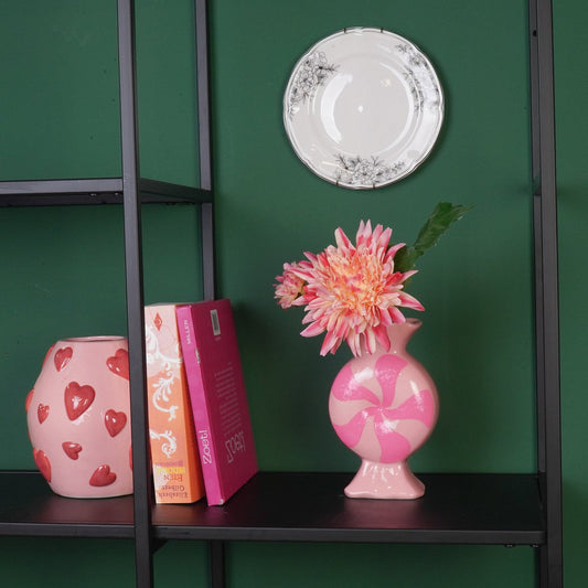 De roze gestreepte vaas in een moderne zwarte metalen kast tegen een groene wand.