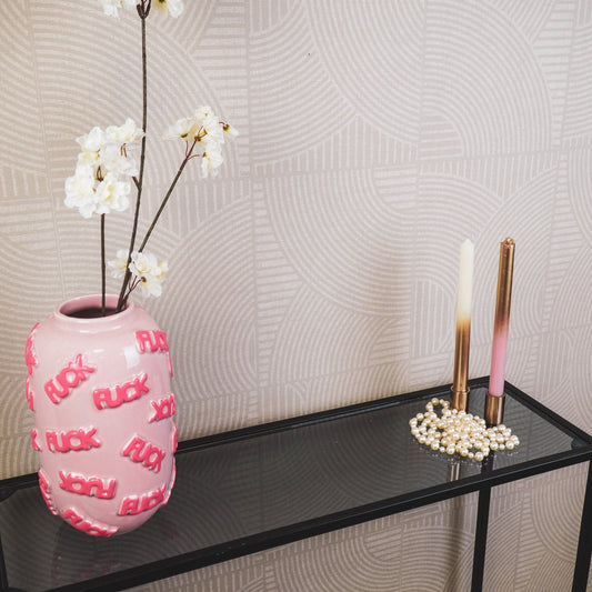 De roze tekstvaas met witte bloemen op een glazen tafel in een licht interieur.