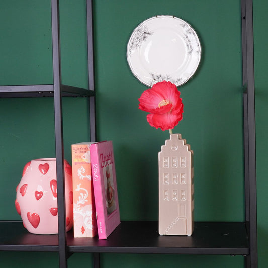 Stylingvoorbeeld van de beige huisvaas met één bloem in een moderne zwarte metalen kast tegen een groene wand.