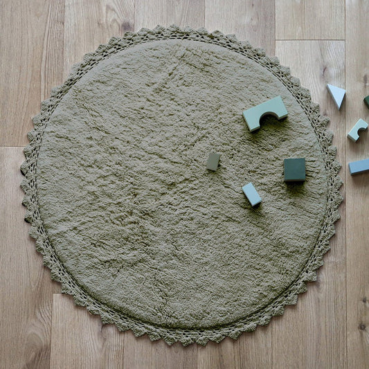 Sfeerafbeelding van het ronde olijfgroene vloerkleed Perla in een kinderkamer met houten bouwblokken als speelkleed.