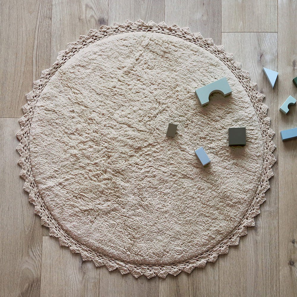 Sfeerafbeelding van het ronde zandbeige vloerkleed Perla in een kinderkamer met houten bouwblokken als veilig speelkleed.