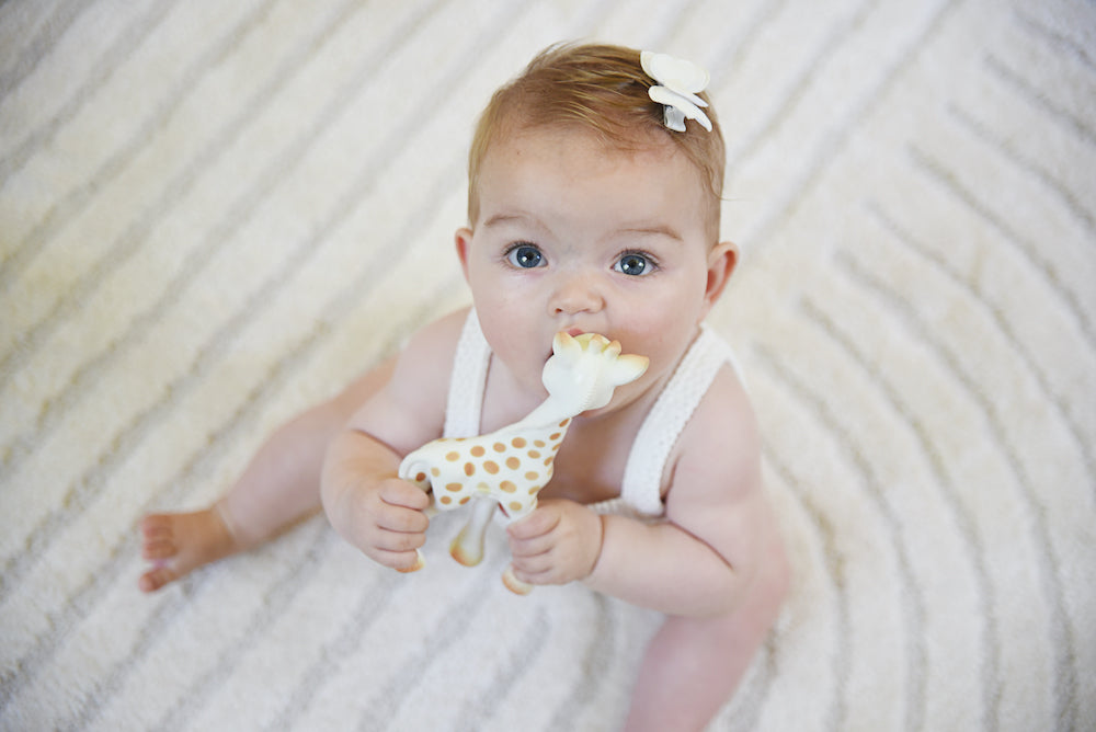Bovenaanzicht van een baby die Sophie de giraf makkelijk vasthoudt aan de lange nek.