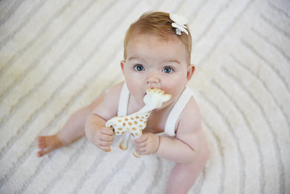 Bovenaanzicht van een baby die Sophie de giraf makkelijk vasthoudt aan de lange nek.