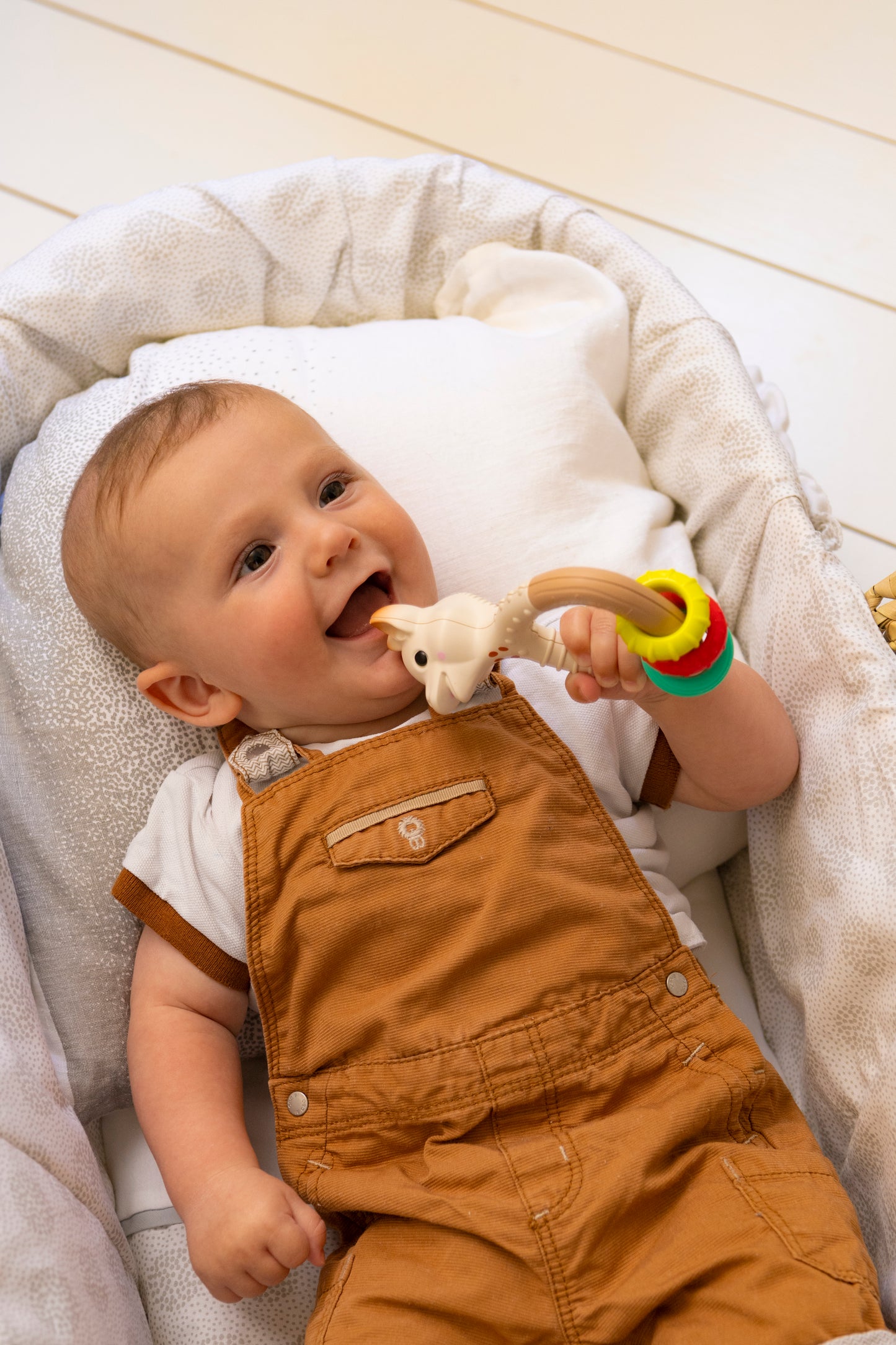 Baby in een wiegje die veilig de texturen van de Natur’rings rammelaar verkent met de mond.