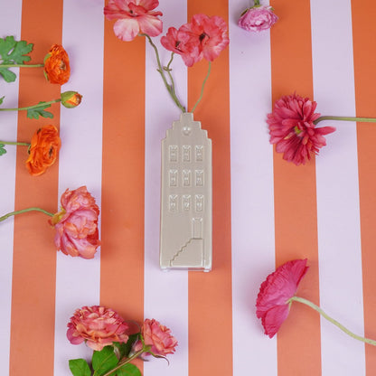 De beige grachtenhuis-vaas liggend op een gestreepte tafel, gevuld met een selectie kleurrijke bloemen.