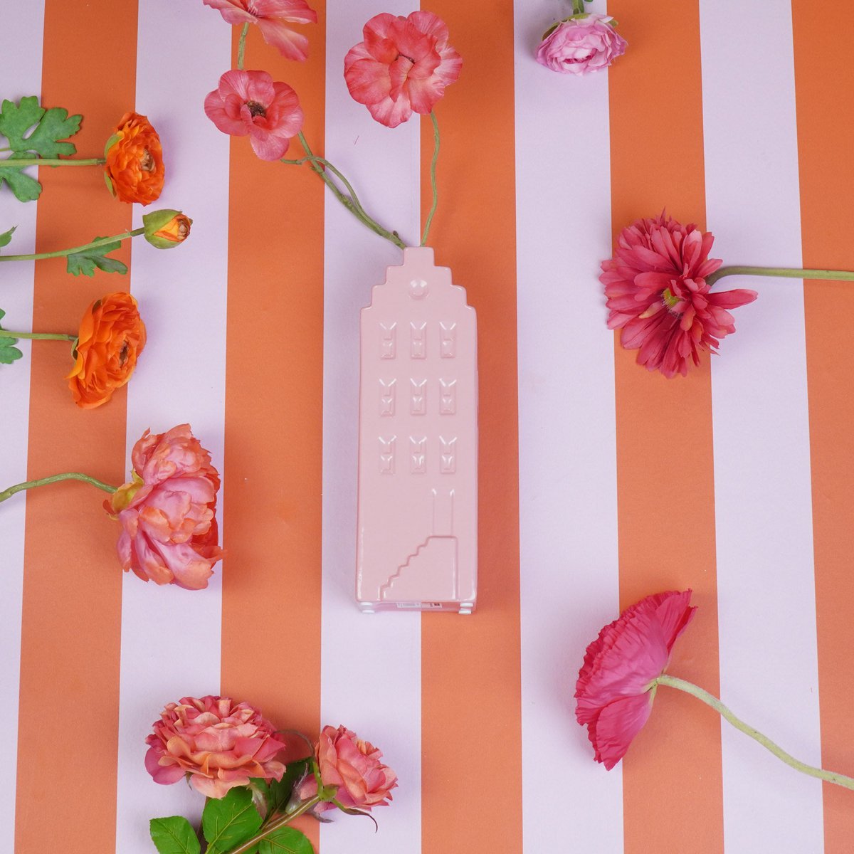 De roze Amsterdamse huisvaas gepresenteerd op een gestreepte tafel met diverse bloemen.