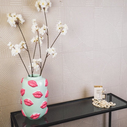 De mintgroene lipvaas met witte bloemen op een glazen tafel tegen een warme beige achtergrond.