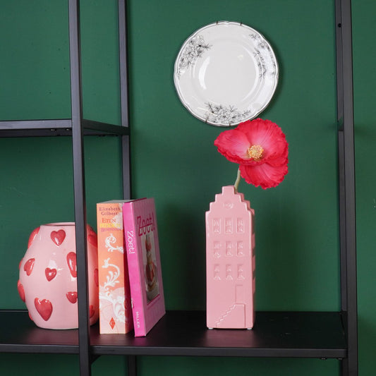 Roze grachtenpand vaas met een bloem in een zwarte metalen kast tegen een groene achtergrond.