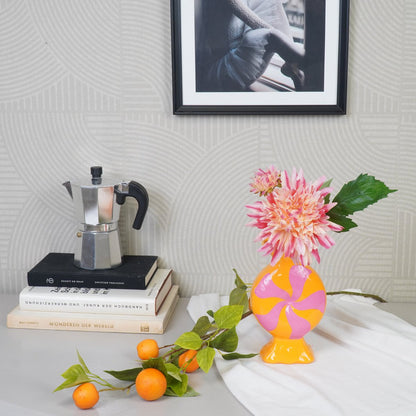 Oranje Toffee Candy vaas met roze bloemen op een bureau naast een tak met mandarijnen.