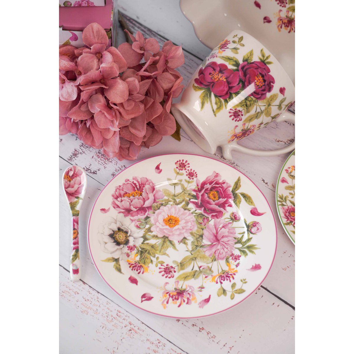 Sfeerimpressie van het Peony dessertbord op een witte houten tafel, gecombineerd met de bijpassende porseleinen kop, lepel en een rode hortensia bloem.