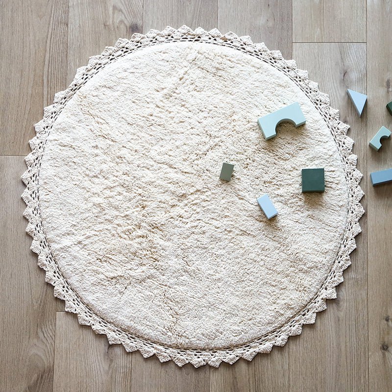 Sfeerafbeelding van het ronde ecru vloerkleed Perla in een kinderkamer met houten bouwblokken als speelkleed.