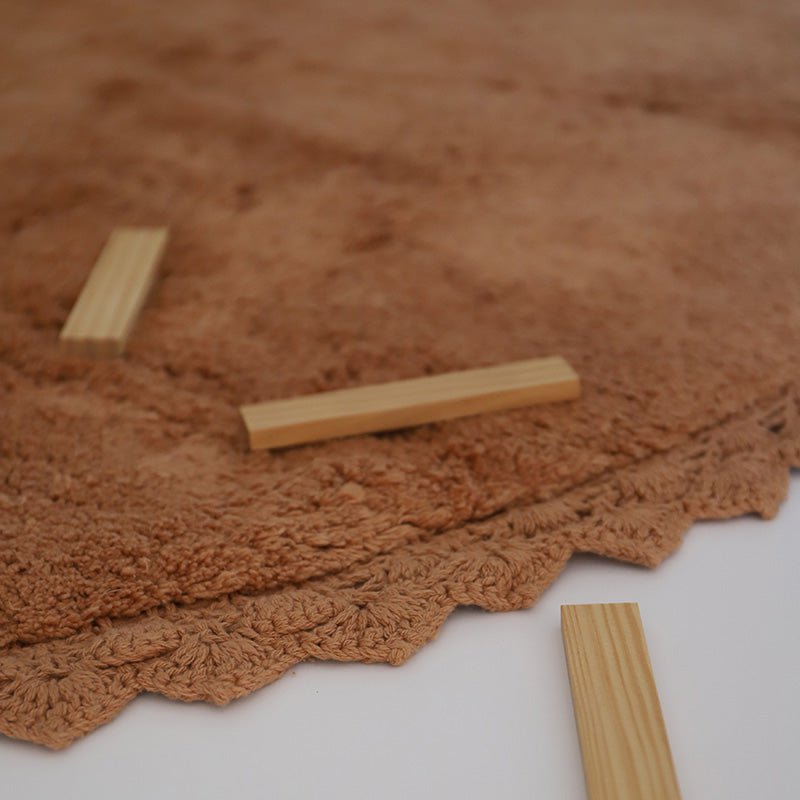 Detailopname van de gehaakte rand van het toffeekleurige Perla vloerkleed met houten speelblokjes erop.