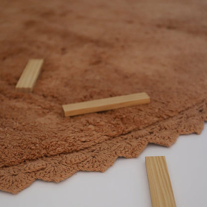 Detailopname van de gehaakte rand van het toffeekleurige Perla vloerkleed met houten speelblokjes erop.