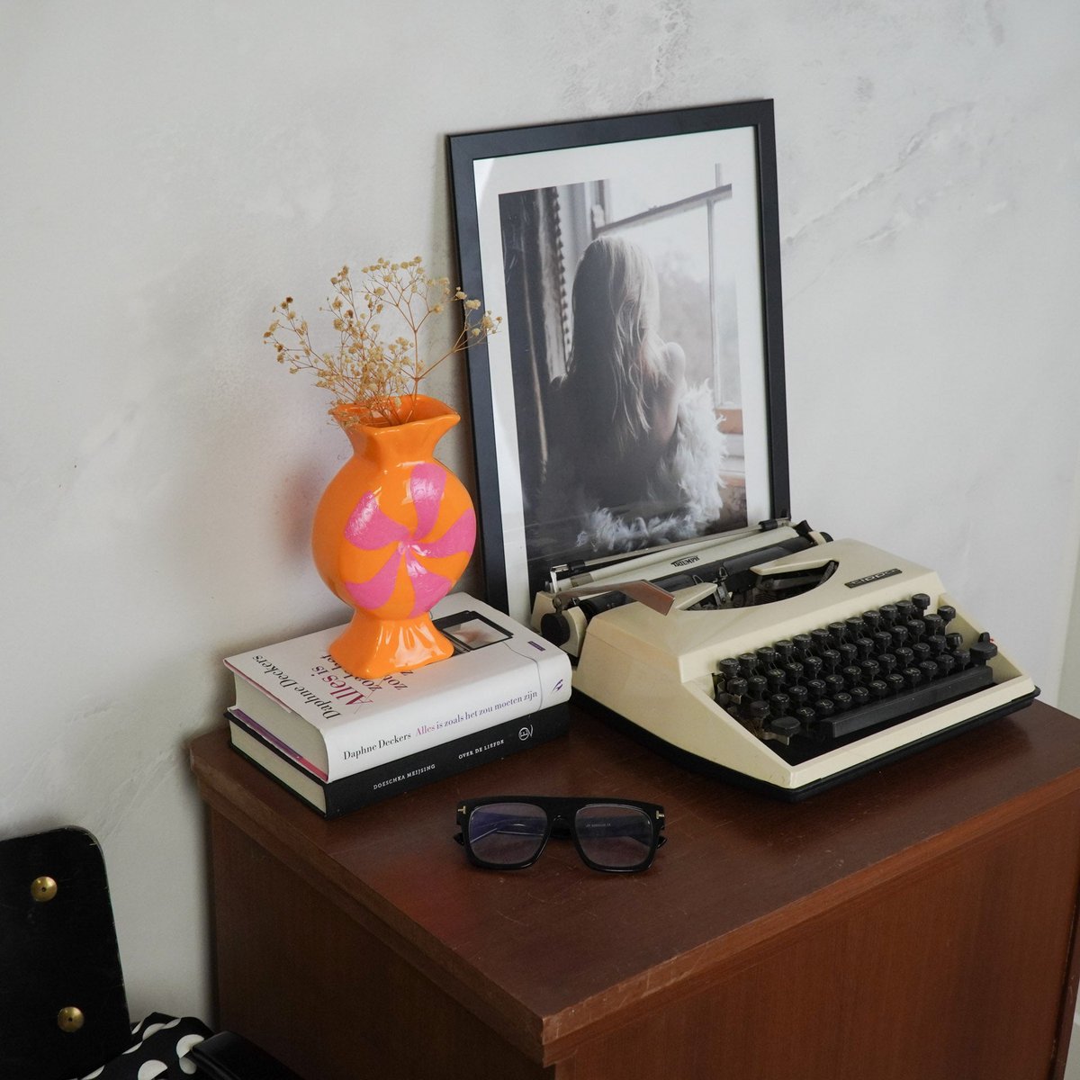 Retro sfeerfoto van de oranje vaas op een stapel boeken naast een oude typemachine op een houten kast.