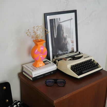 Retro sfeerfoto van de oranje vaas op een stapel boeken naast een oude typemachine op een houten kast.